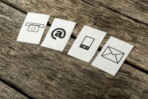 Contact and communication icons telephone at sign mobile and mail on four white cards spread over textured rustic wooden boards.